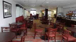 A hotel dining area with multiple tables and chairs, a red sofa, and a kitchen area in the background.