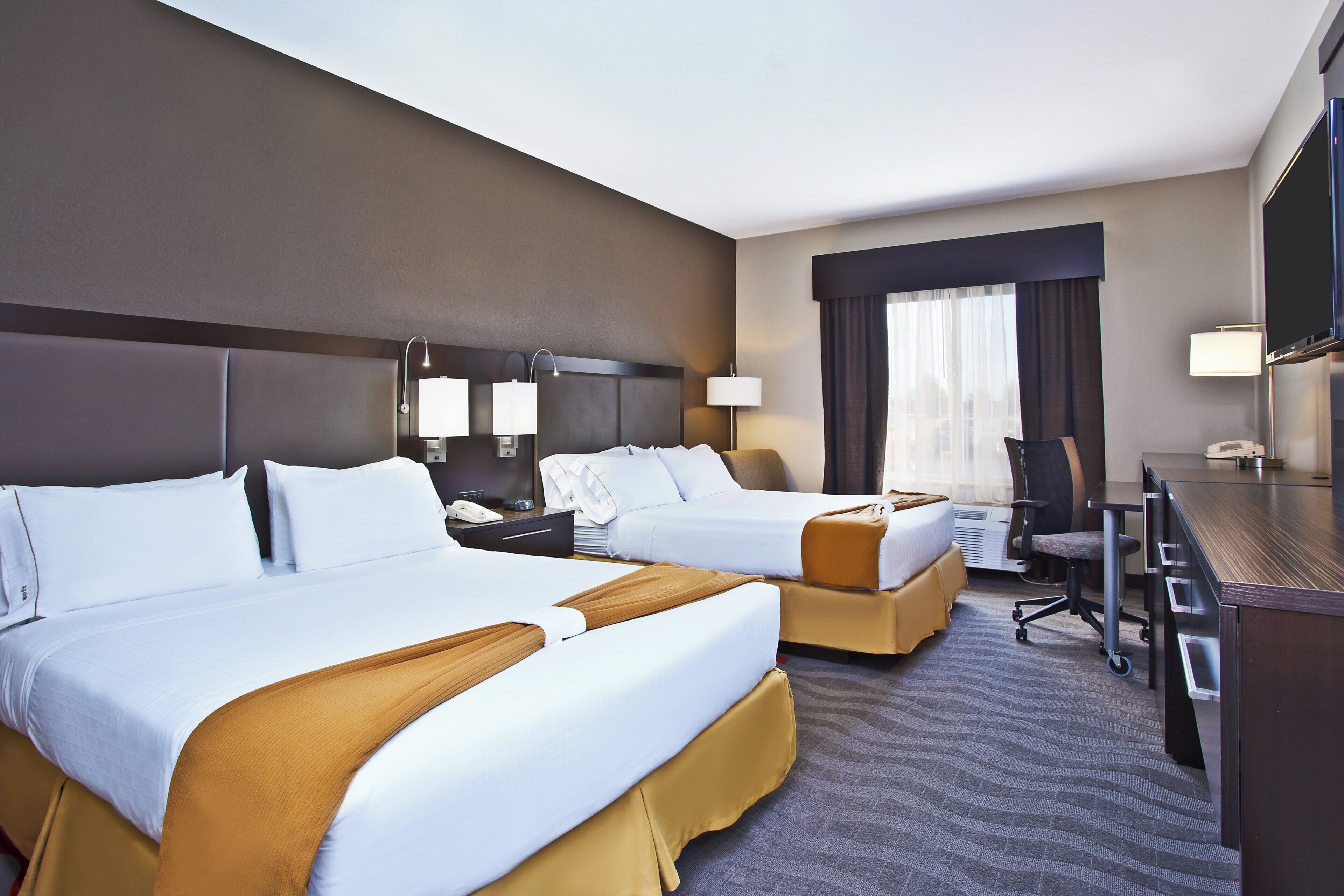 A hotel room with two beds, a desk, a chair, and a television.