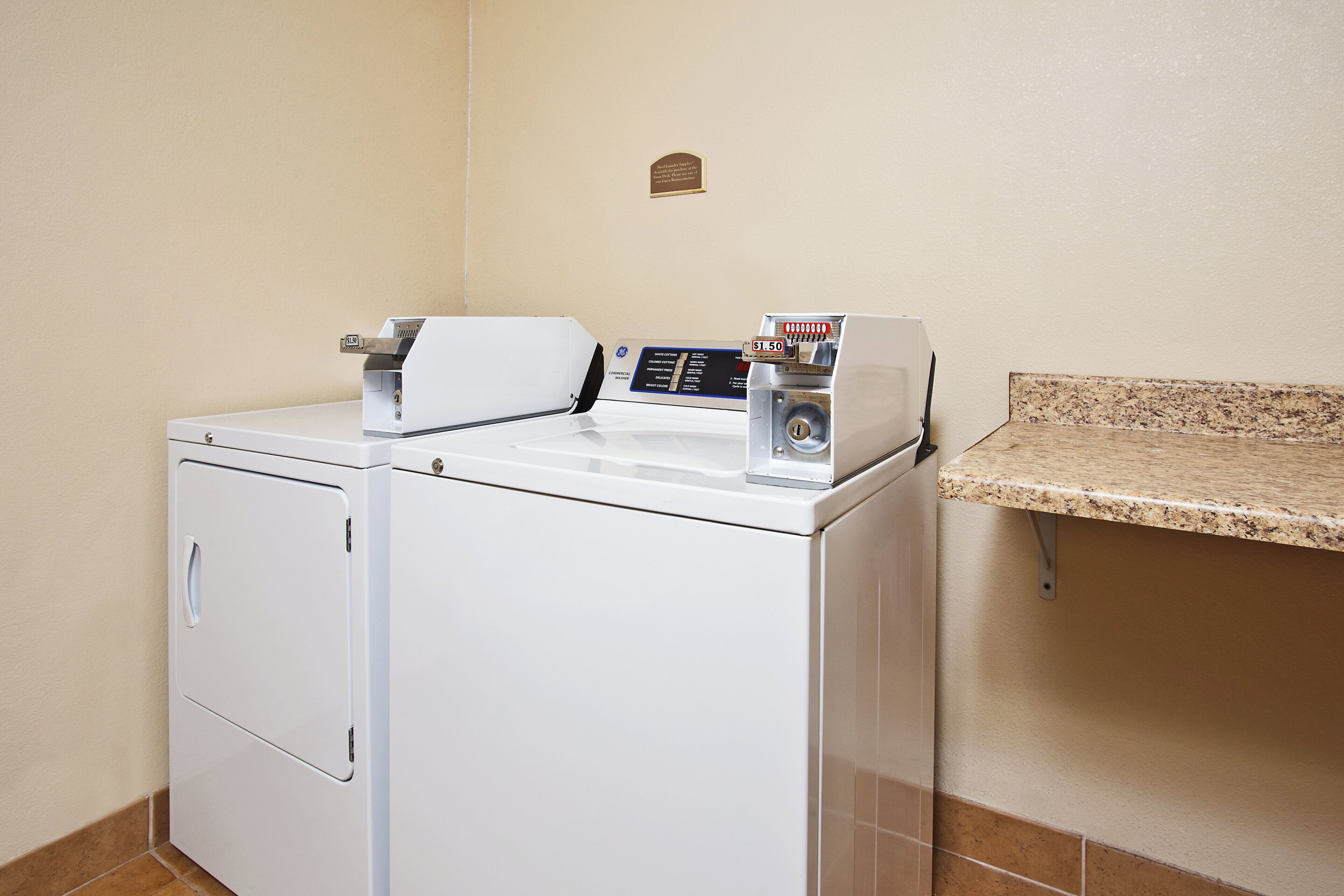 A front-loading washer and dryer unit with a control panel and a coin-operated dryer on top.