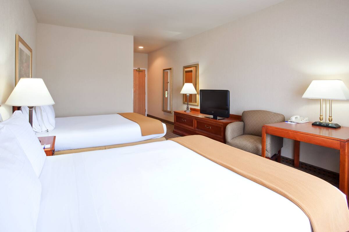 A hotel room with two beds, a television, a desk, and a chair.