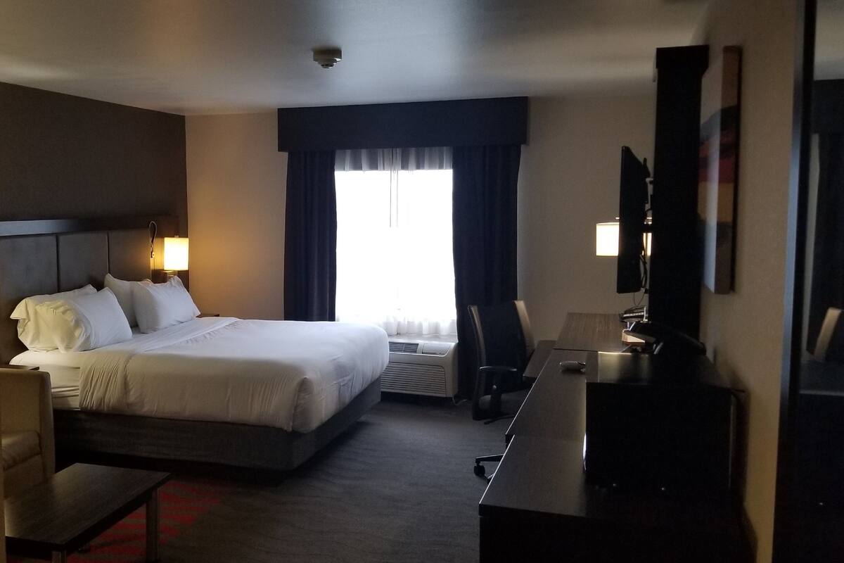 A hotel room with a large bed, a desk, a chair, a TV, and a window with curtains.