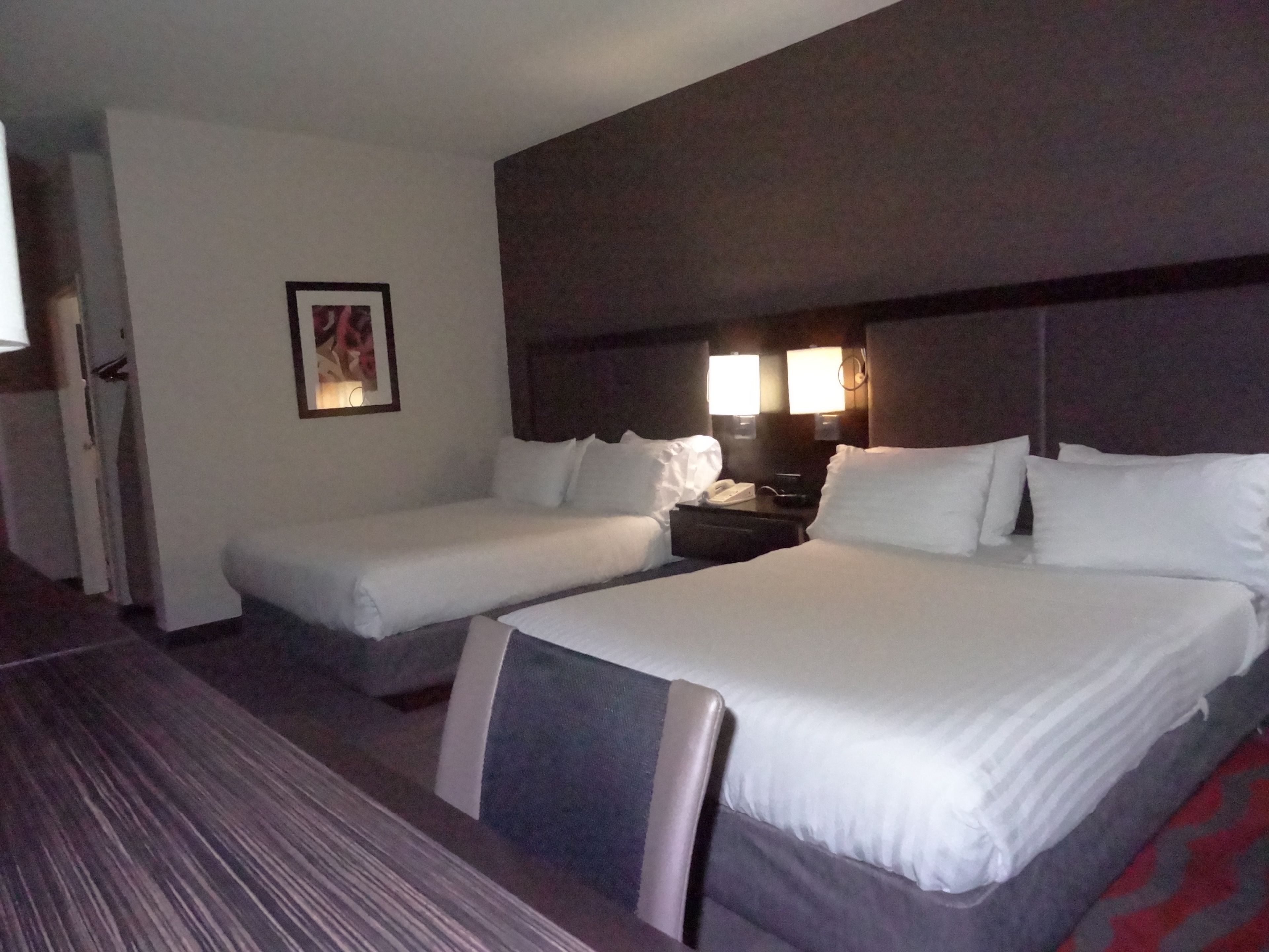 A hotel room with two beds, a nightstand with a phone, and a framed picture on the wall.