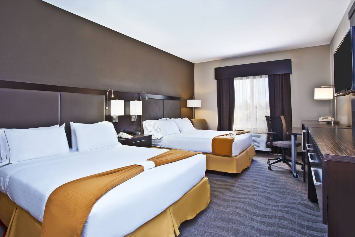 A hotel room with two beds, a desk, a chair, and a television.