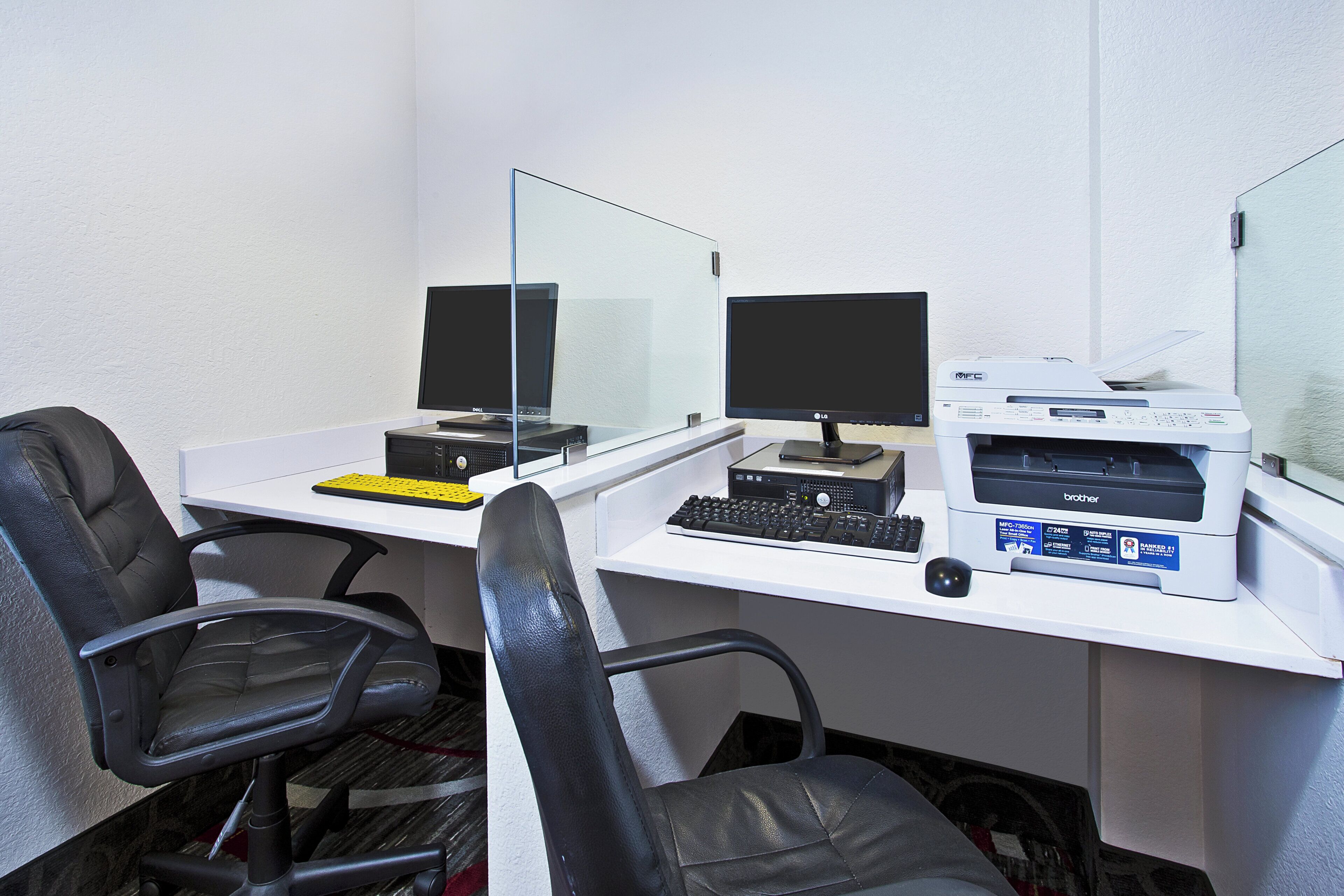 A workspace with two computer monitors, a keyboard, and a printer on a white desk. There are two black office chairs.