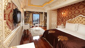 A luxurious hotel room with ornate gold and red wallpaper, a large bed with a dark brown bedspread, and a view of a cityscape through a window. - Deluxe Golden Horn Sultanahmet Hotel (Istanbul)