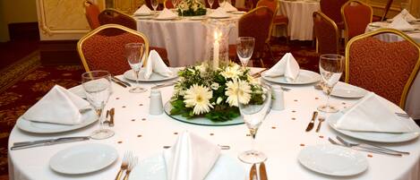 A banquet hall with round tables set for dining, featuring white tablecloths, floral centerpieces, and formal table settings.