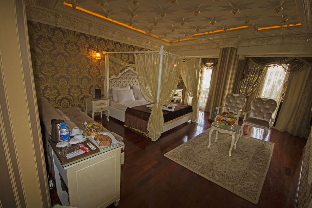Une chambre luxueuse avec un lit à baldaquin, un coin salon avec un fauteuil et une petite table avec des commodités.