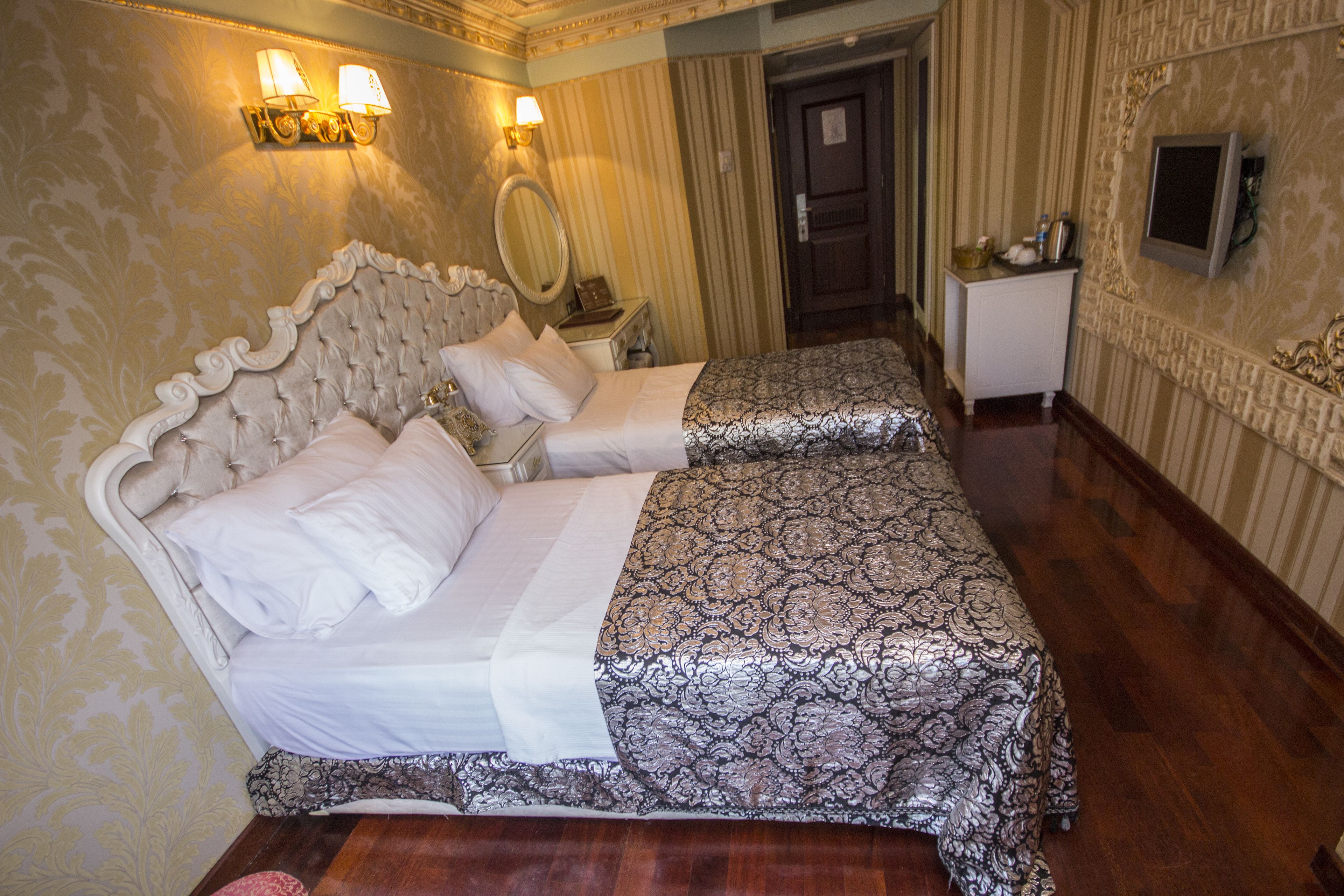 A double bed with a tufted headboard, two bedside tables, a mirror, and a television on a stand.