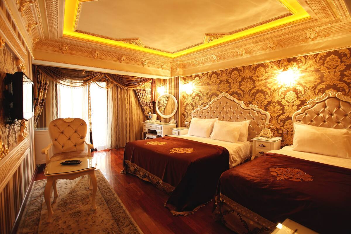 Une chambre à coucher luxueuse, dotée de deux lits, de décorations murales raffinées et d’un lustre classique.