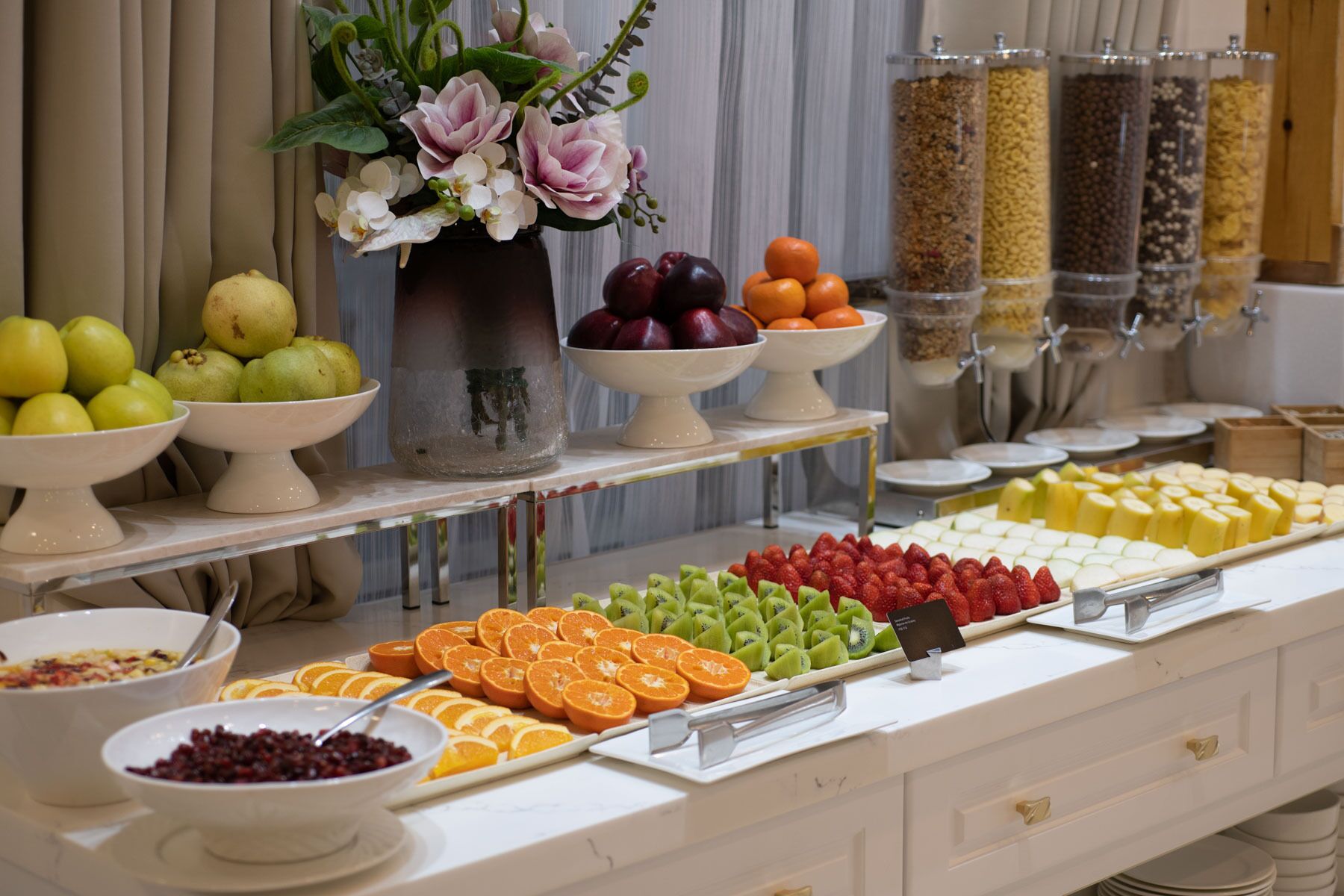 Un bufé con diversas frutas, verduras y un jarrón de flores.