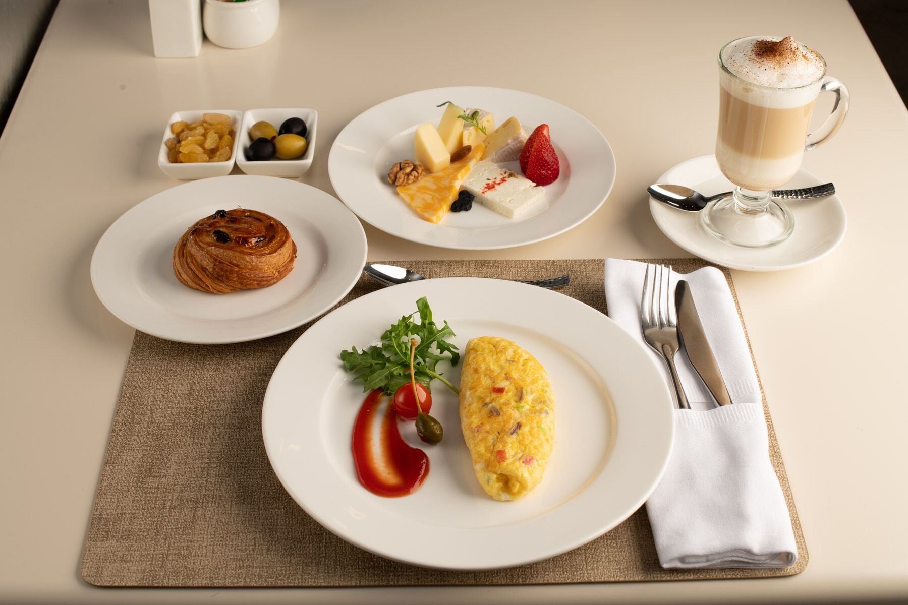 A breakfast setting with a croissant, omelette, fruit, and coffee on a table.