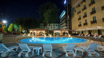 A nighttime pool area with lounge chairs and a building with balconies in the background.