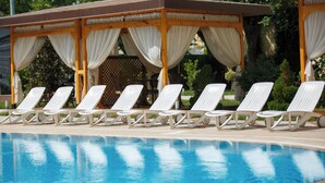 Zona de piscina con sillones blancos y un área de estar cubierta con cortinas blancas.