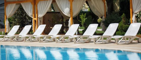 Zona de piscina con sillones blancos y un área de estar cubierta con cortinas blancas.