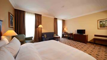 A hotel room with a large bed, a desk with a chair, a television, and a sofa.