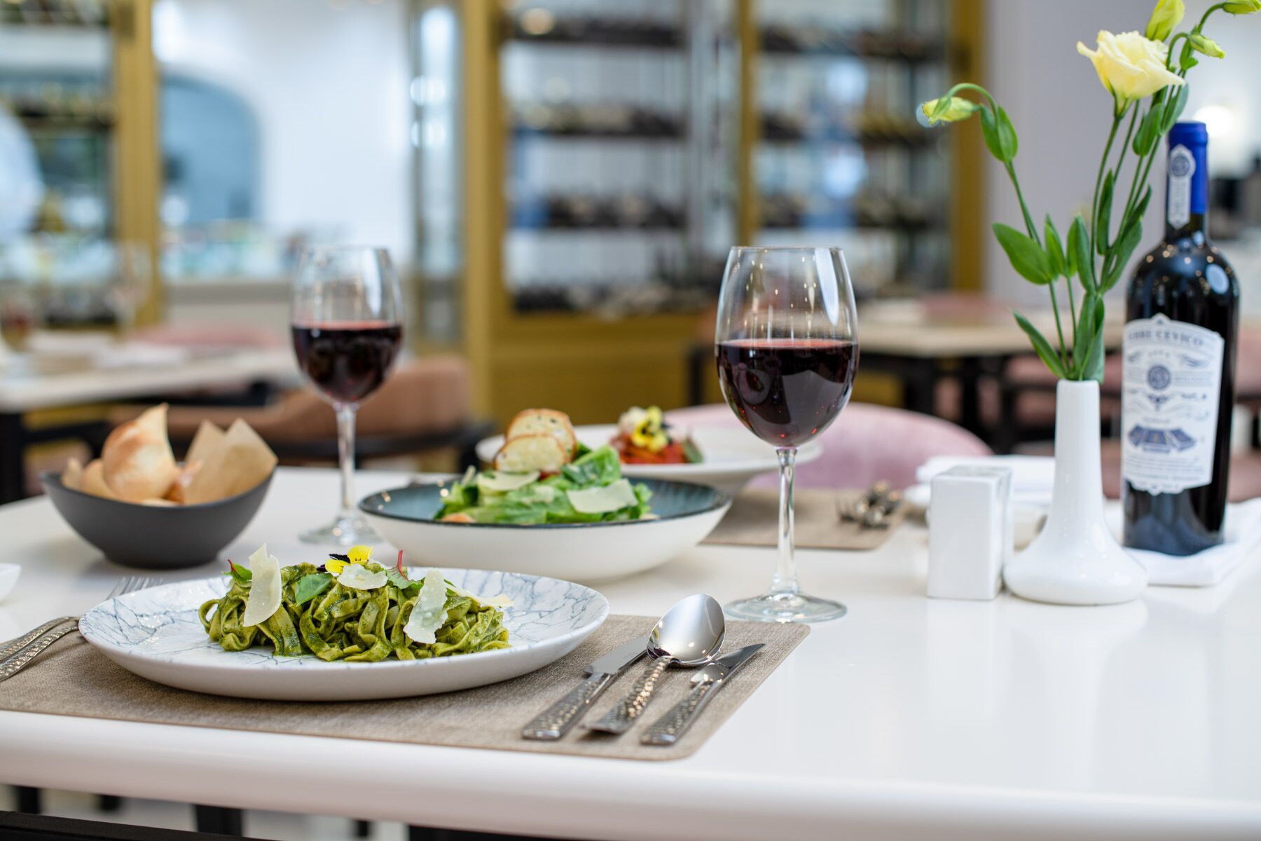 A dining table with plates of food, wine glasses, and a bottle of wine.