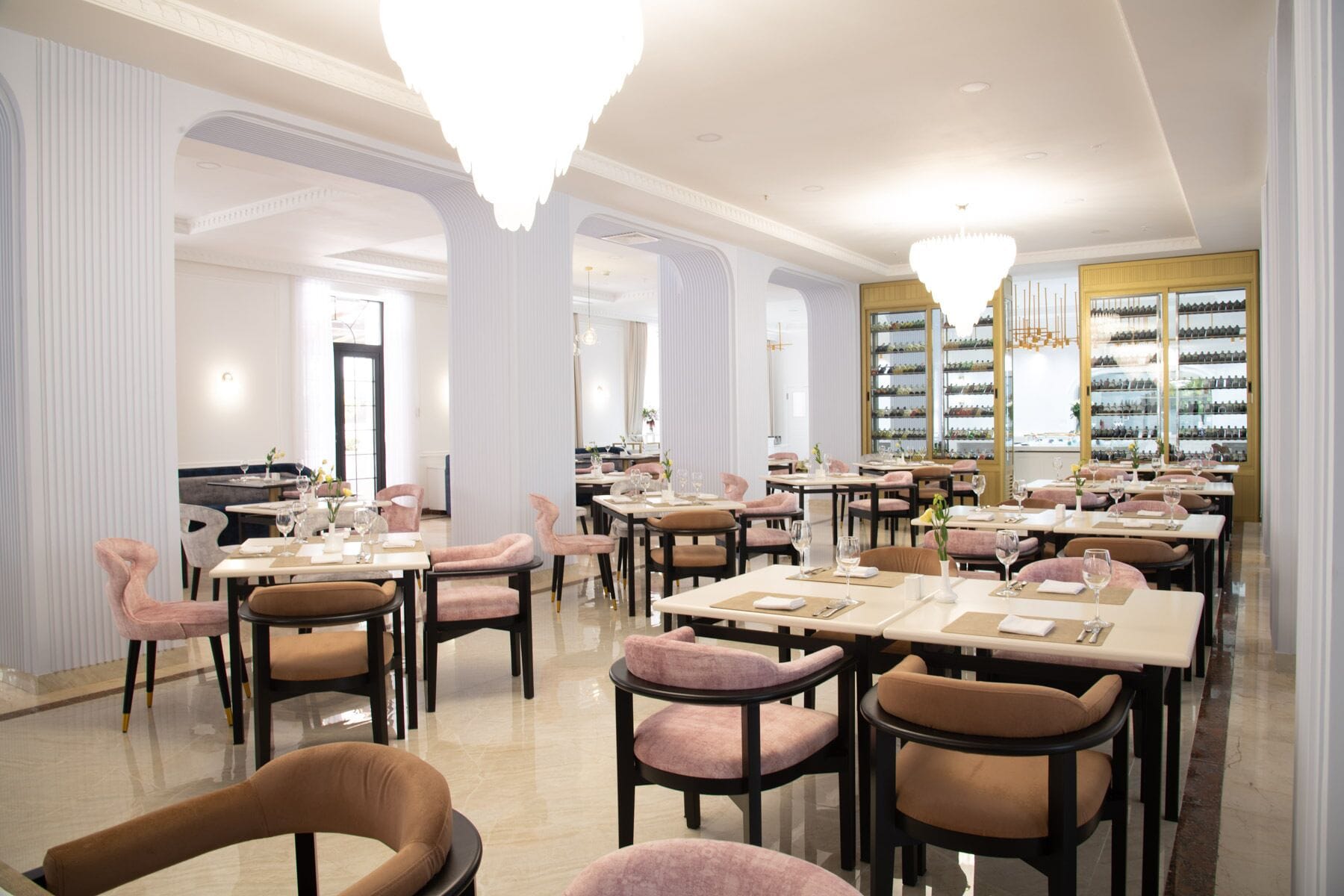 A restaurant with multiple dining tables and chairs, a chandelier, and a wine display.