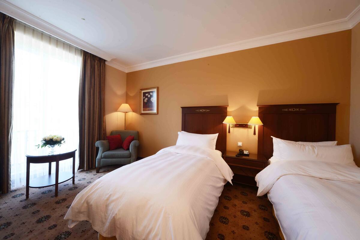Habitación de hotel con dos camas, un escritorio, una silla y una lámpara.