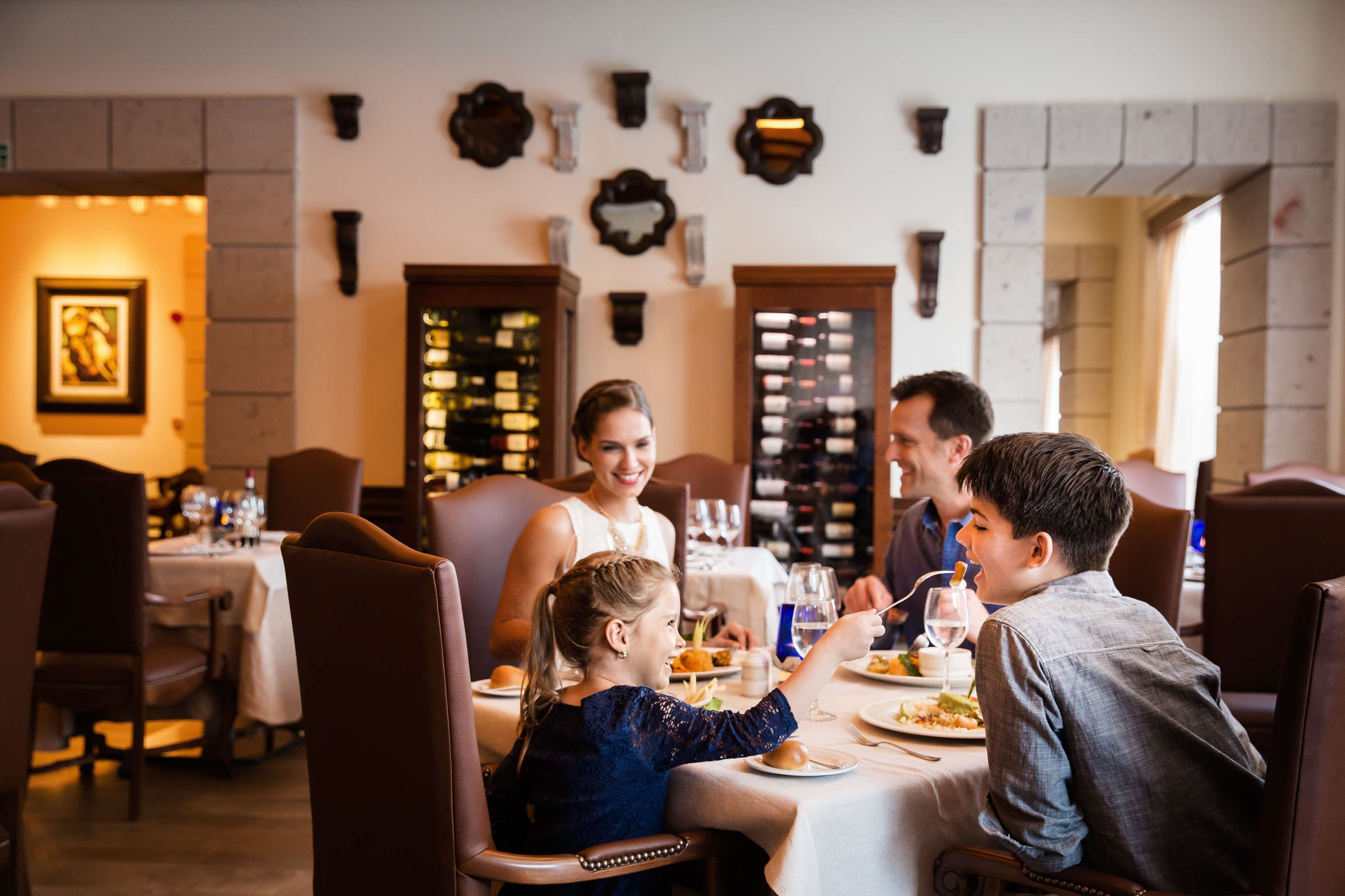 Eine Familie isst in einem Restaurant mit weißem Tischtuch, Weingläsern und verschiedenen Gerichten.