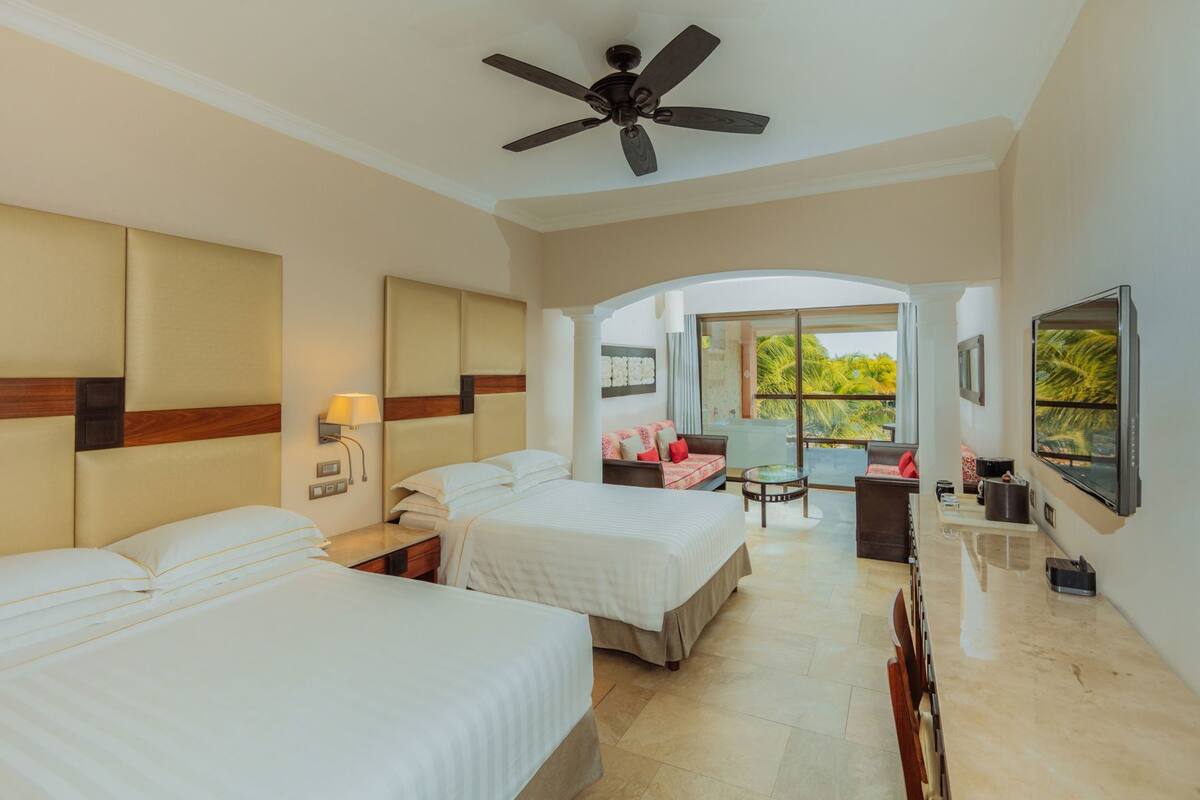 A hotel room with two beds, a ceiling fan, a balcony with a view, and a TV.