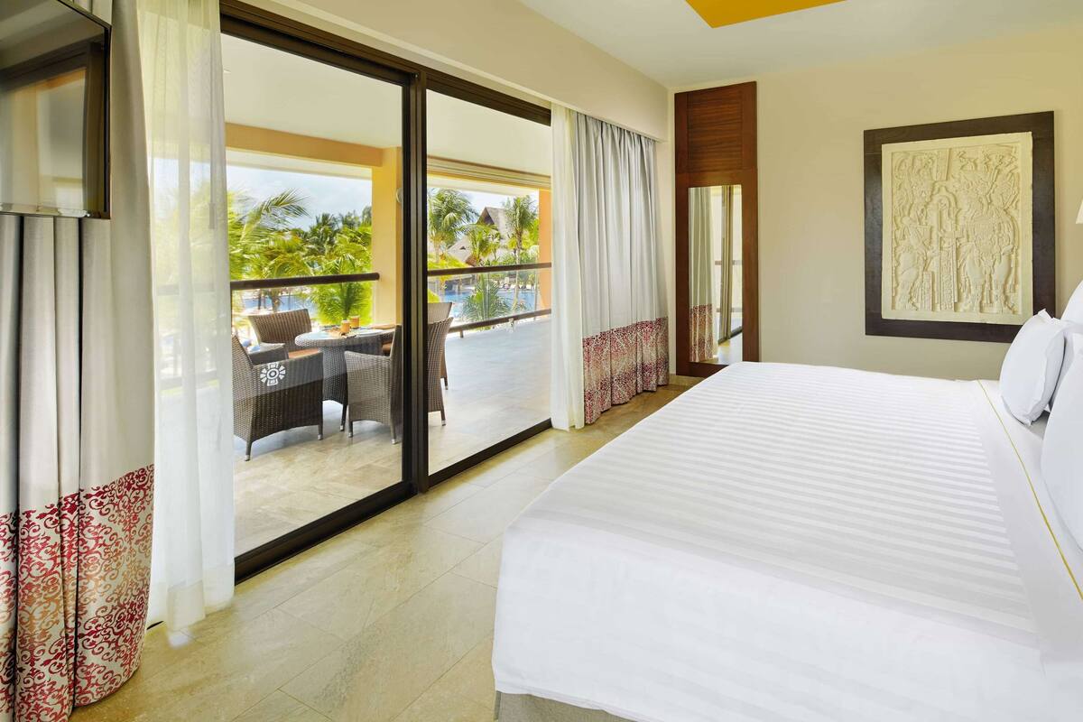 Una habitación de hotel con una cama grande, un balcón con mesa y sillas, y un elemento decorativo en la pared.
