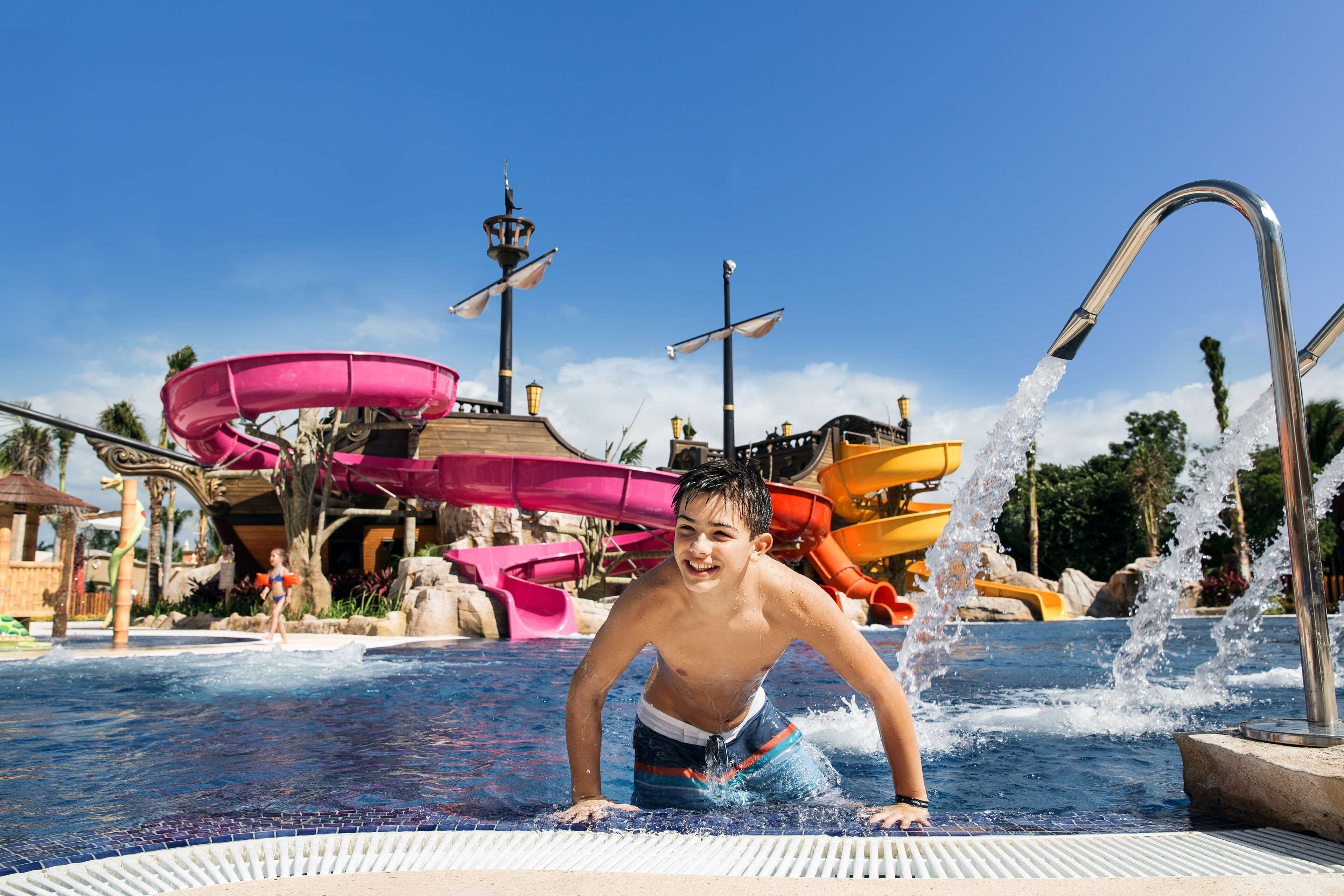 A pool area with water slides and a ship-themed structure in the background.