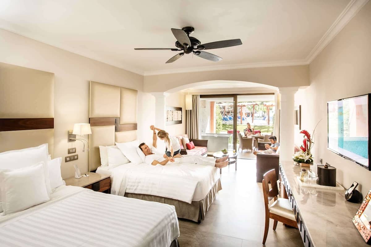 Habitación de hotel con dos camas, un escritorio, una silla, un televisor y un ventilador de techo.