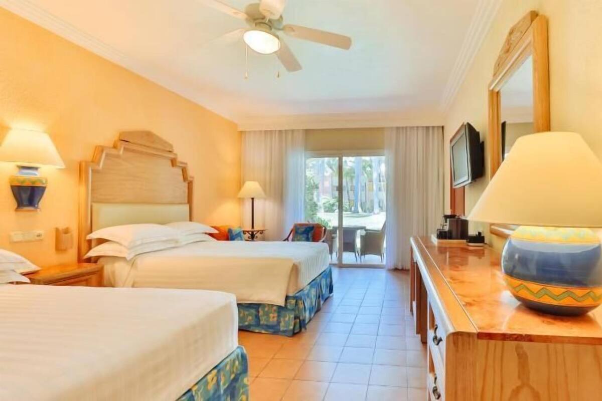 A hotel room with two beds, a ceiling fan, a TV, and a view of the outdoors.