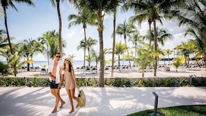 Una pareja caminando por un sendero en la playa, con palmeras y sillas de descanso al fondo.