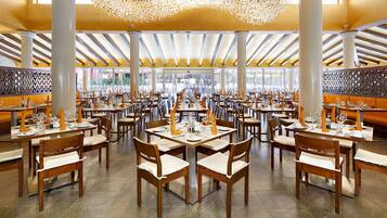 A spacious dining area with multiple tables and chairs, large windows, and a decorative chandelier.