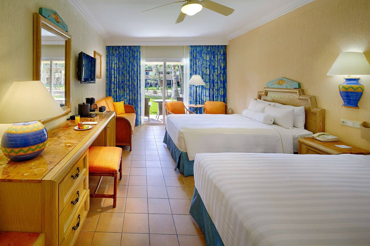 Habitación de hotel con dos camas, un escritorio con lámpara, una silla, un televisor y vistas al exterior.
