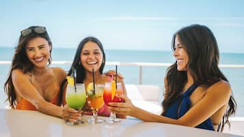 Drie vrouwen zitten aan een tafel met drankjes, met uitzicht op een wateroppervlak.