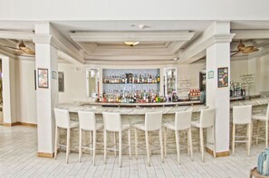 A bar area with a marble countertop, white bar stools, and a variety of bottles and glasses.