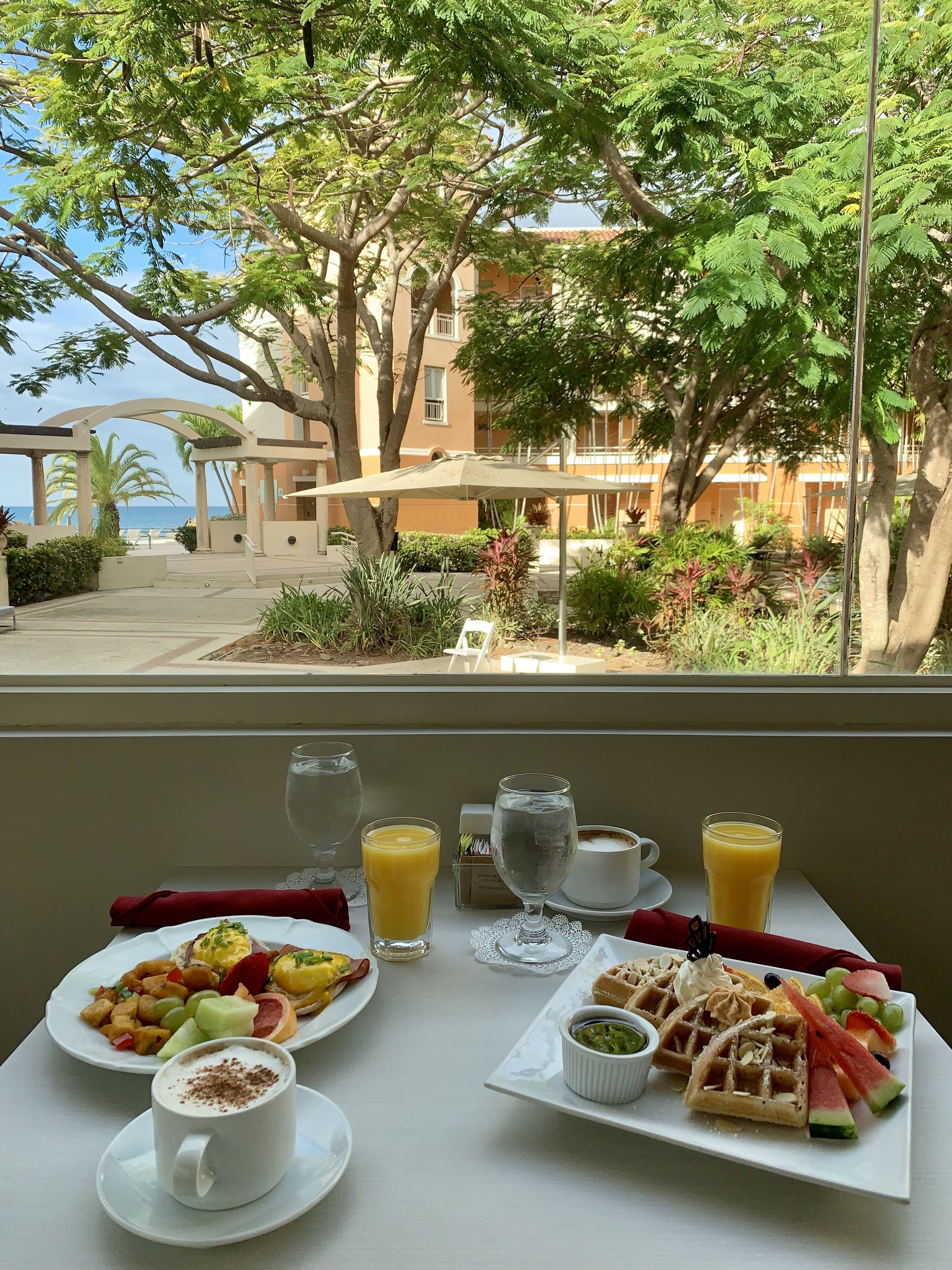 A breakfast table with various dishes and drinks, overlooking a building and a view of the sea.