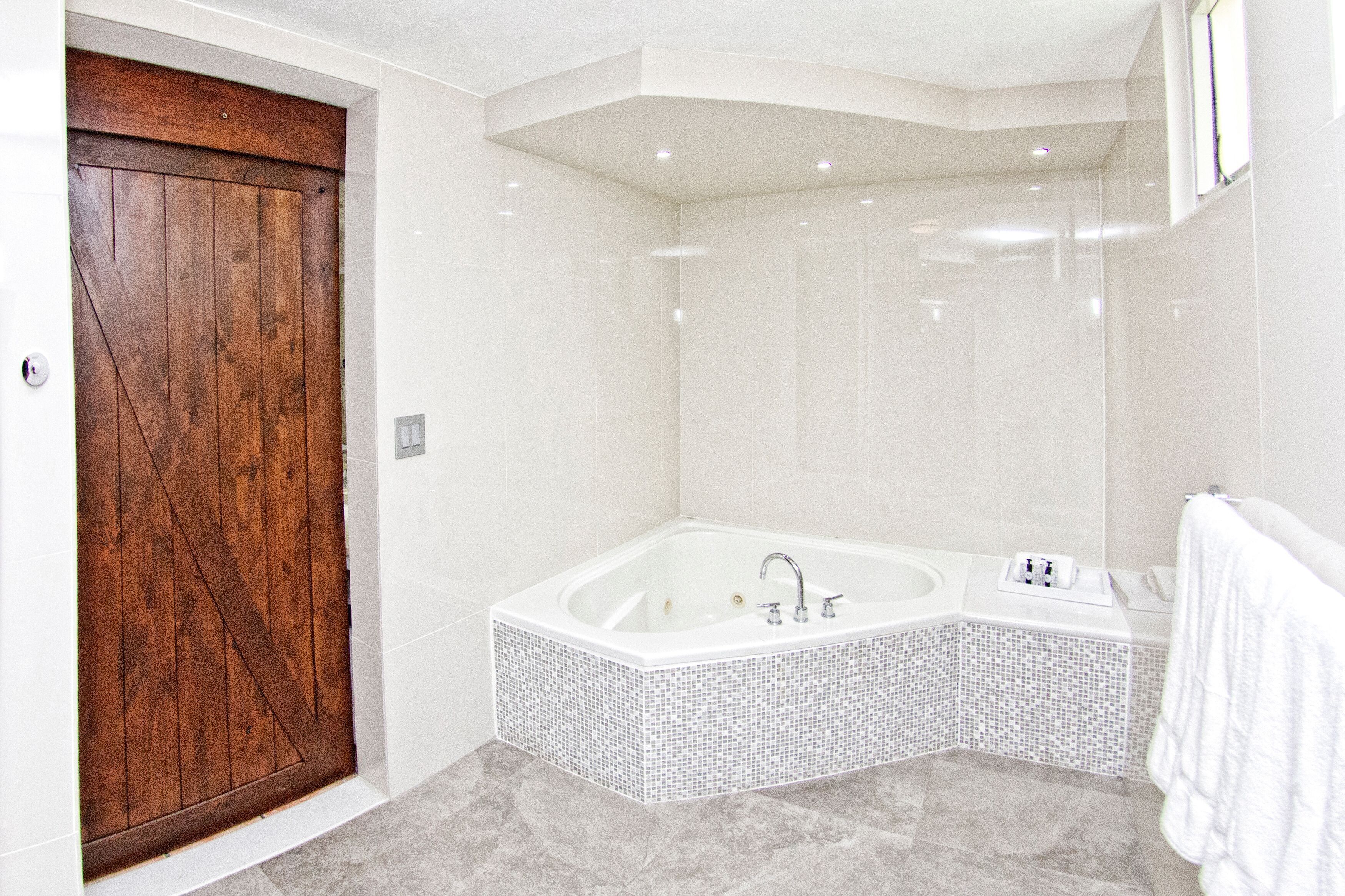 Une salle de bain moderne avec un grand jacuzzi carré, une porte en bois et une douche carrelée de blanc.