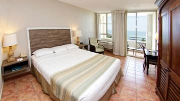 Habitación de hotel con una cama grande, un escritorio, una silla y vista al mar.