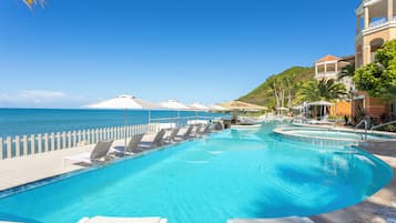 Ein Poolbereich mit Liegestühlen und Sonnenschirmen, freier Blick auf das Meer und ein Gebäude mit Balkonen.