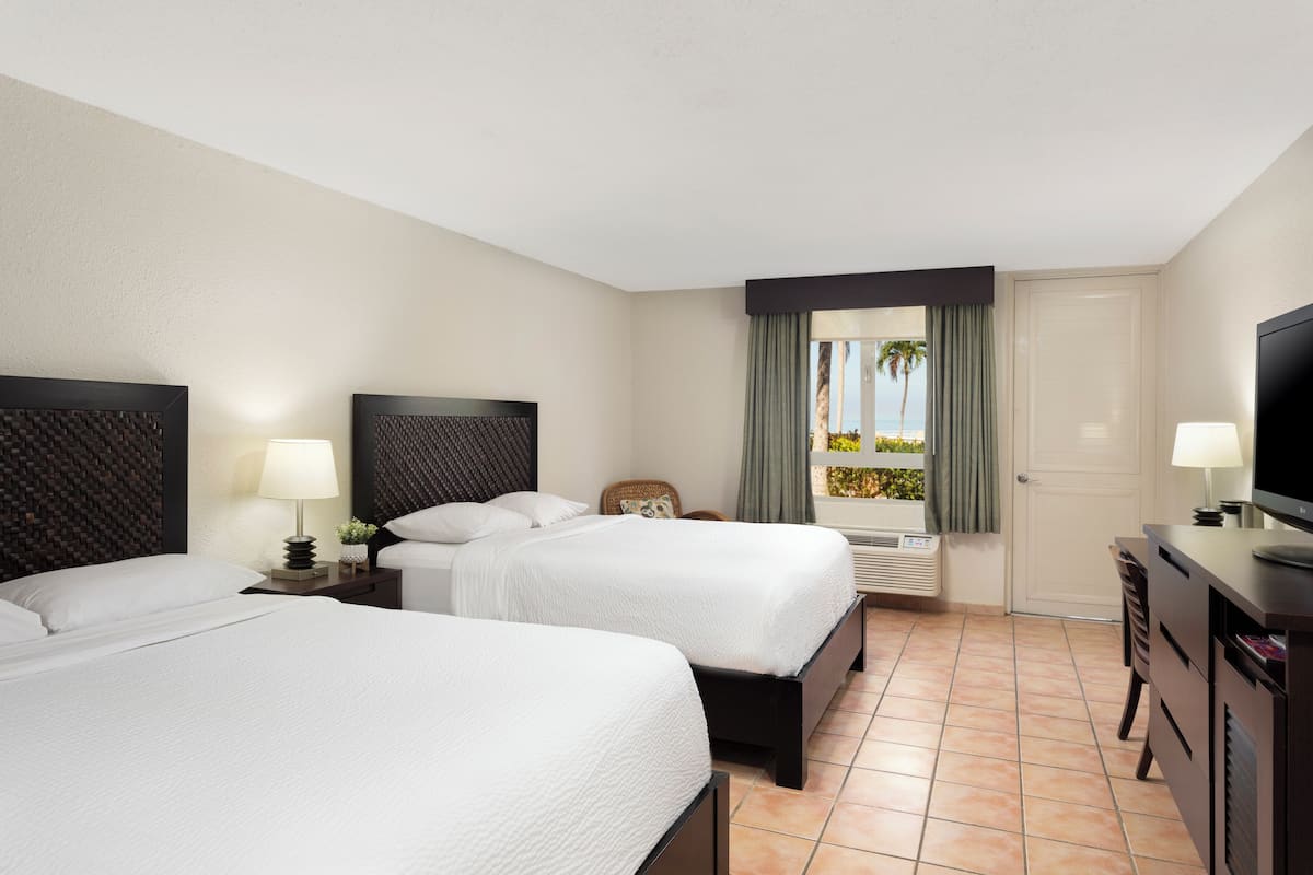 A hotel room with two beds, a television, a desk, and a window with curtains.