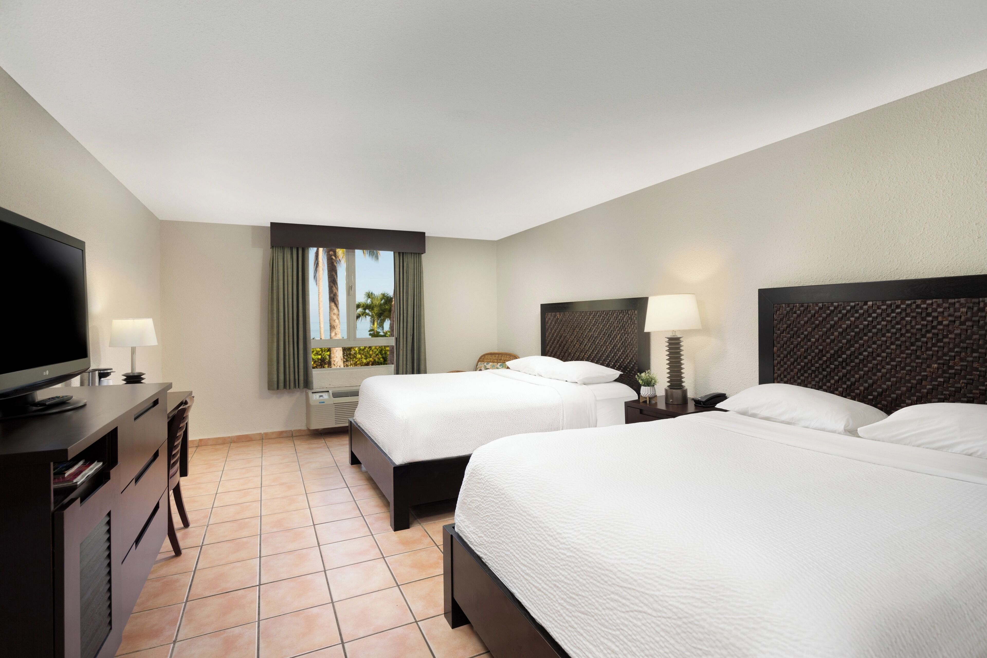 Habitación de hotel con dos camas, televisión, escritorio y ventana con cortinas.