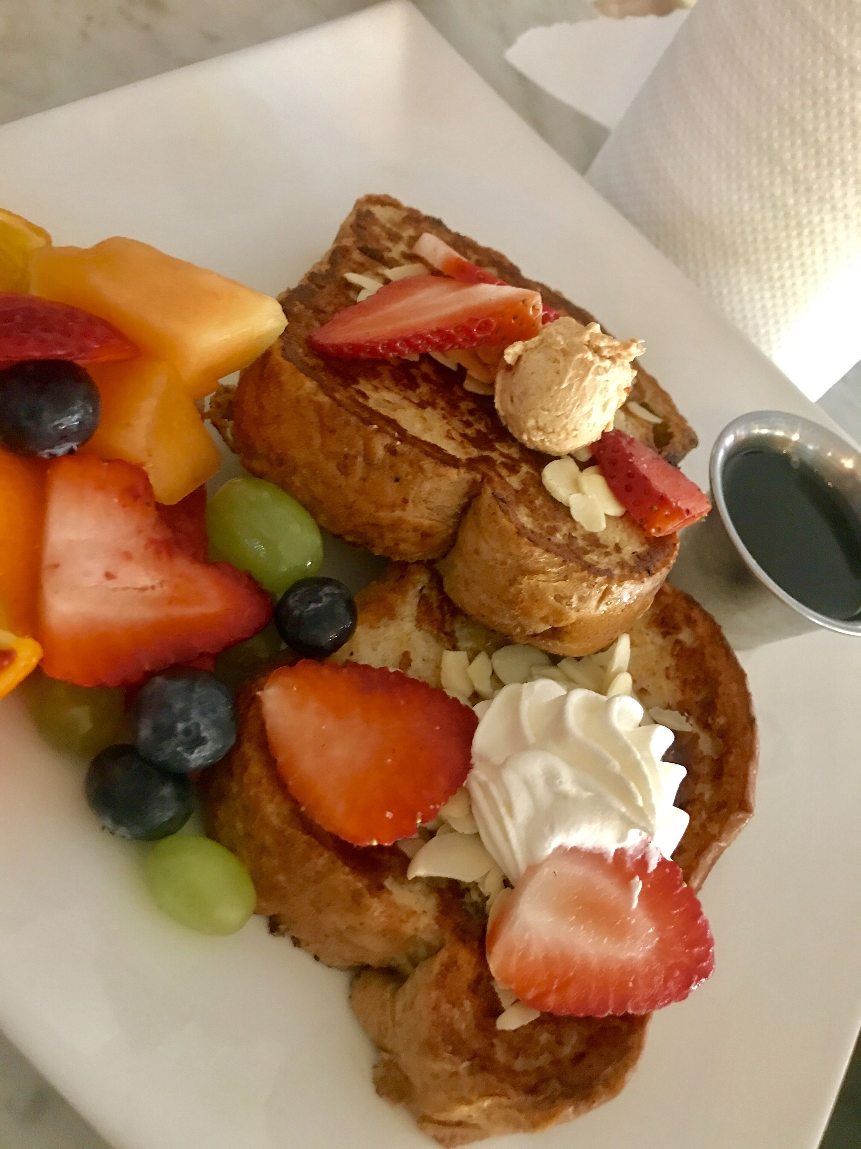 Un plato de tostadas francesas con fresas, arándanos y un recipiente pequeño de almíbar.