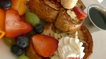 Un plato de tostadas francesas con fresas, arándanos y un recipiente pequeño de almíbar.