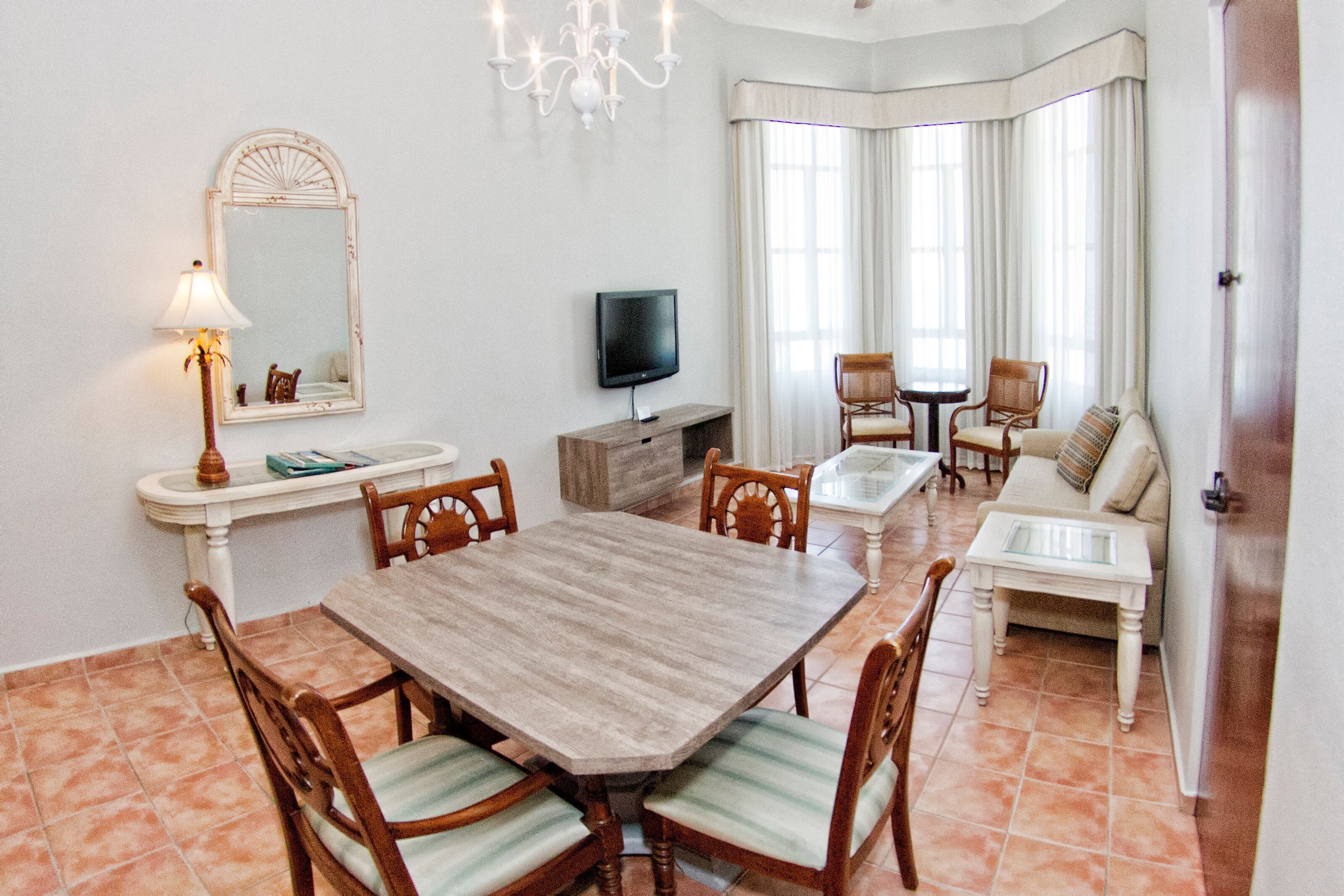 A dining area with a wooden table and chairs, a television, and a sofa with a cushion.