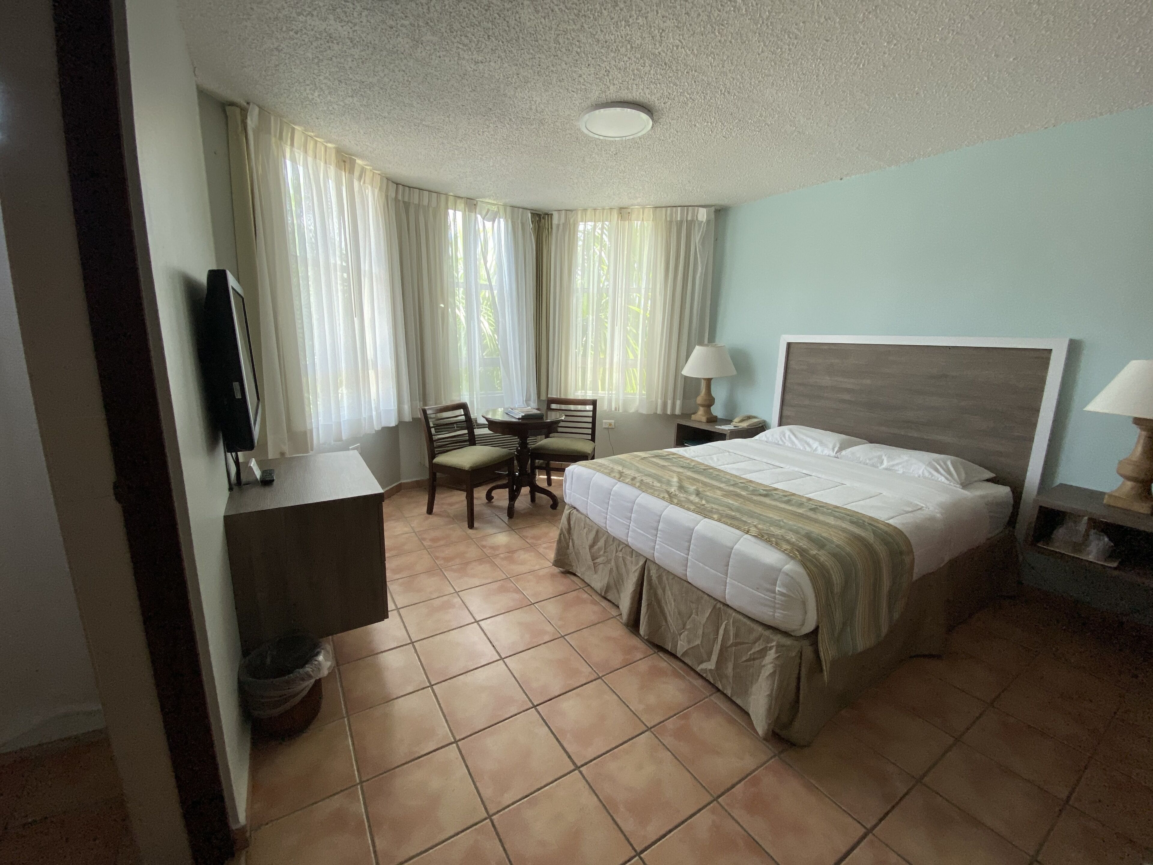 A hotel room with a bed, a desk, a chair, a TV, and a lamp.