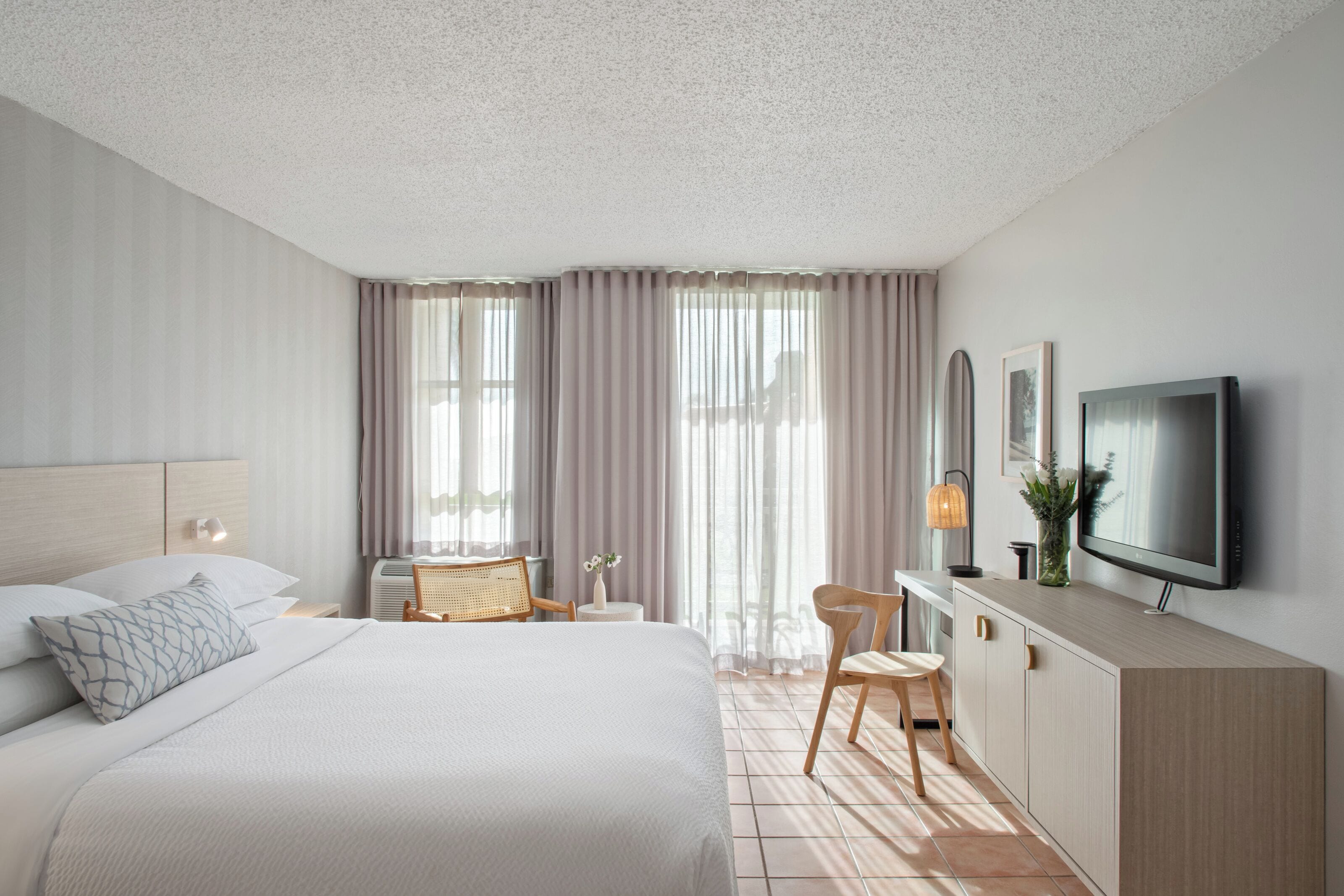 Een moderne hotelkamer met een groot bed, een bureau, een stoel, een televisie en een raam met gordijnen.