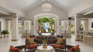 A spacious indoor area with a high ceiling, a central seating area with round tables and chairs, and a view of a beach through an archway. - Rincon Beach Resort (Añasco)