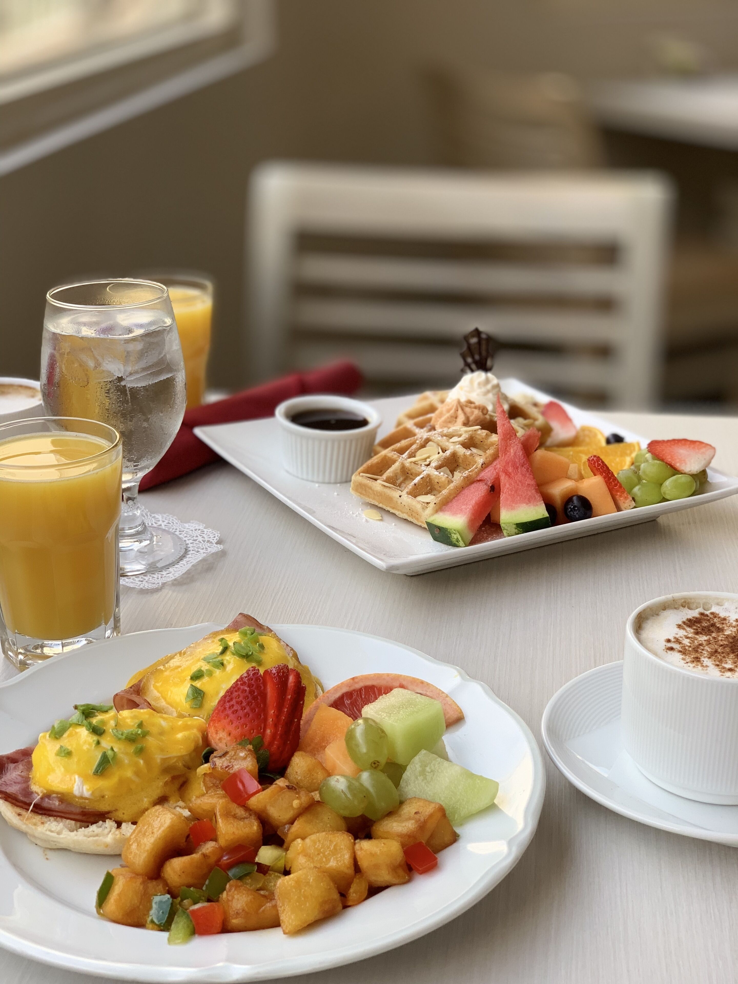 Une table dressée pour le petit-déjeuner, avec des gaufres, des fruits et des boissons.