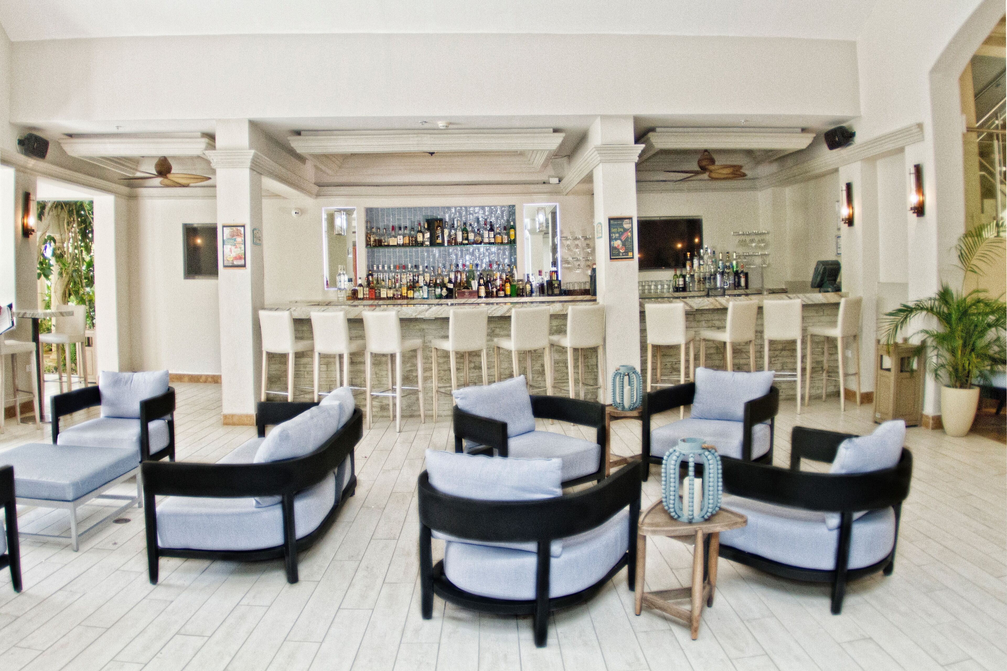 A bar area with multiple seating options, including lounge chairs and bar stools, and a well-stocked bar counter.