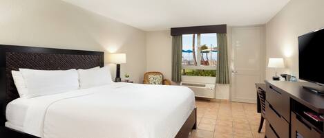 A hotel room with a large bed, a television, a desk with a computer, and a window with a view of the beach.
