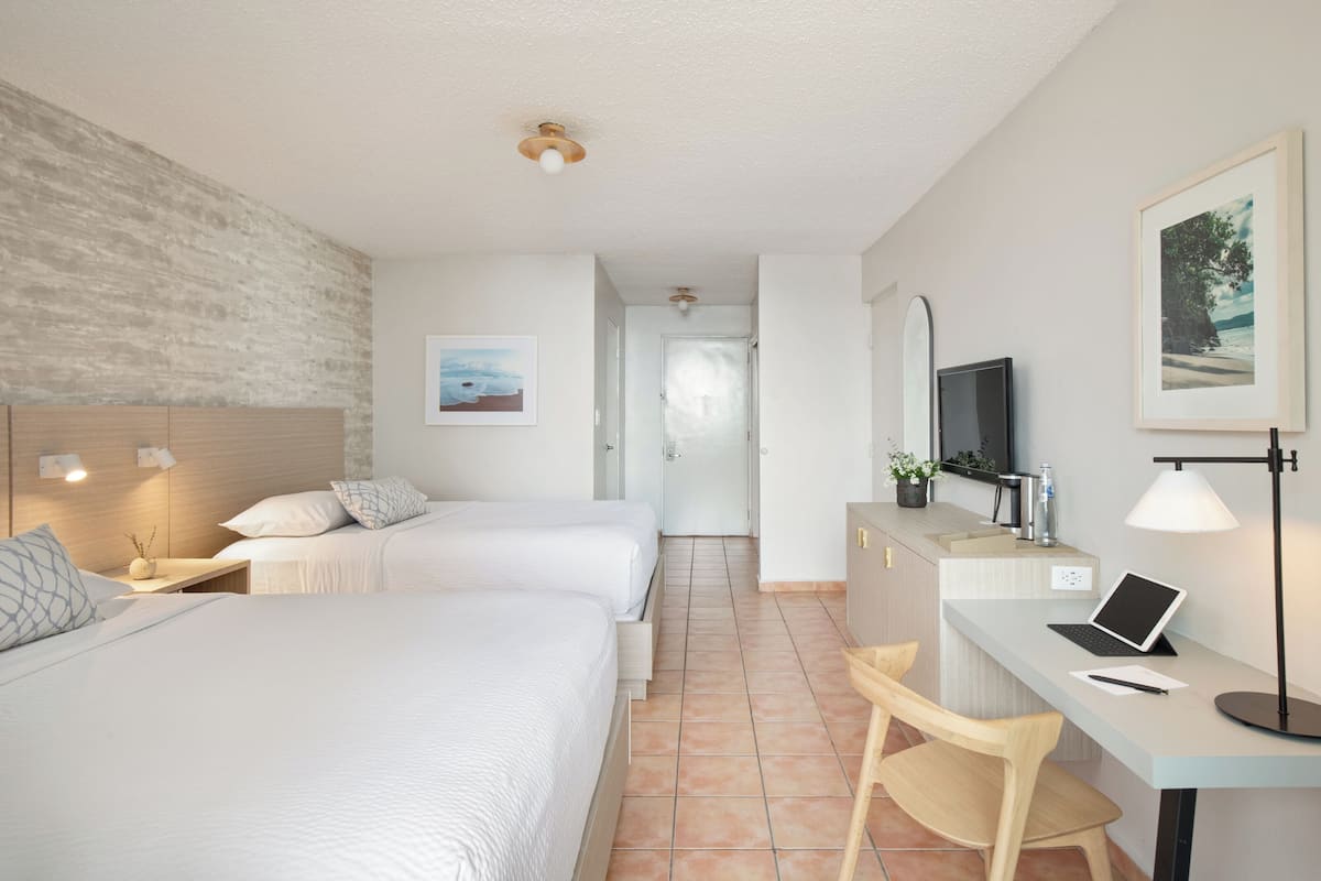 A hotel room with two beds, a desk with a laptop, a chair, a TV, and a framed picture on the wall.