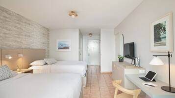 A hotel room with two beds, a desk with a laptop, a chair, a TV, and a framed picture on the wall.